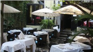 Un espace de restauration en plein air avec des tables et des chaises, des parasols et un escalier menant à un niveau supérieur.
