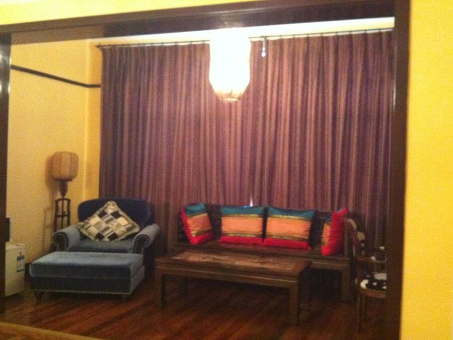 Uma sala de estar com sofá, banquinho e abajur.