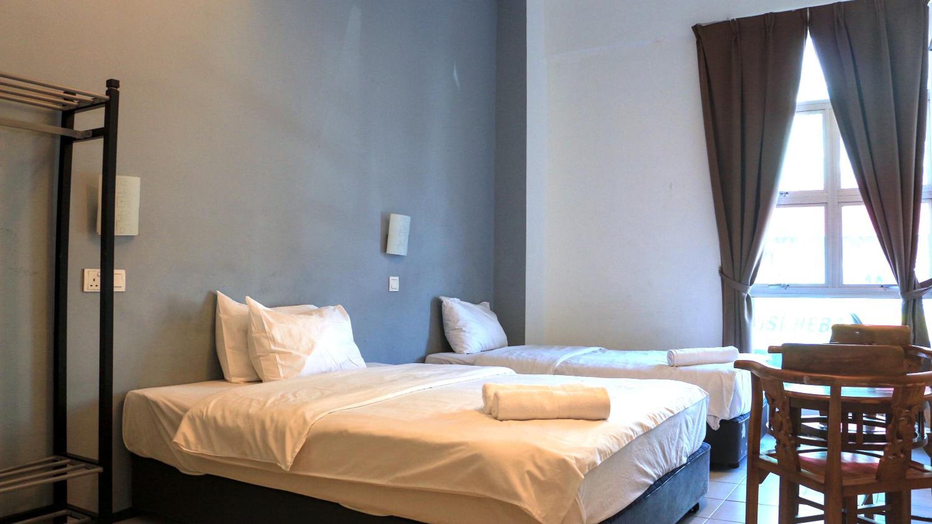 A hotel room with two beds, a chair, and a window with curtains.