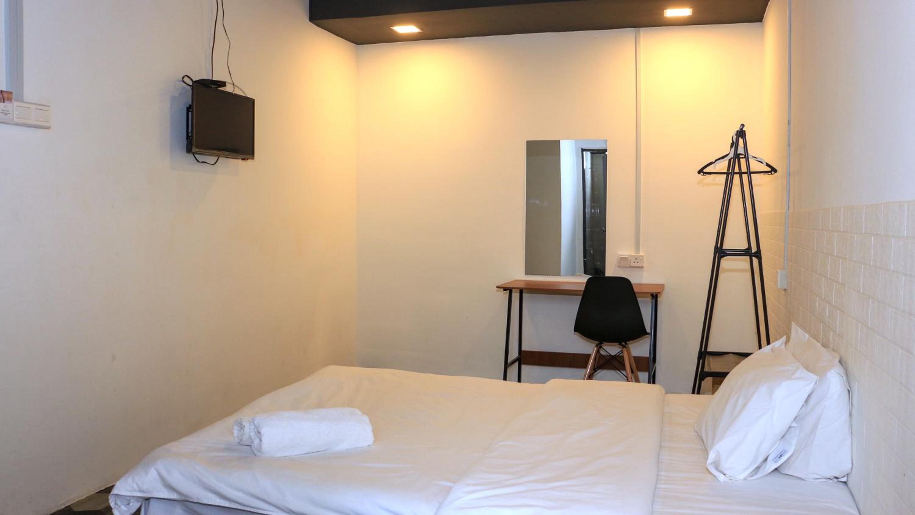 A hotel room with a bed, a desk, a chair, a ladder, and a mirror.
