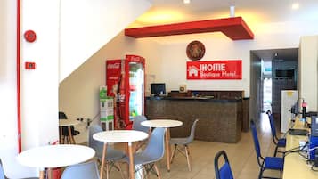 A hotel lobby with a reception desk, a Coca-Cola refrigerator, and seating area with tables and chairs.