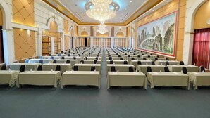 A large conference room with rows of tables, a chandelier, and a large painting on the wall. - Sabai Hotel (Nakhon Ratchasima)