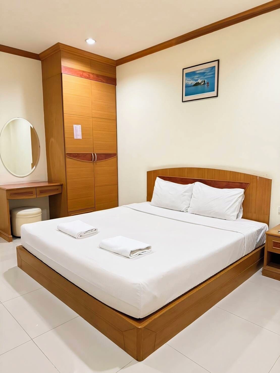 Une chambre d’hôtel avec un grand lit, une tête de lit en bois, un miroir rond, une armoire et un tableau encadré au mur.