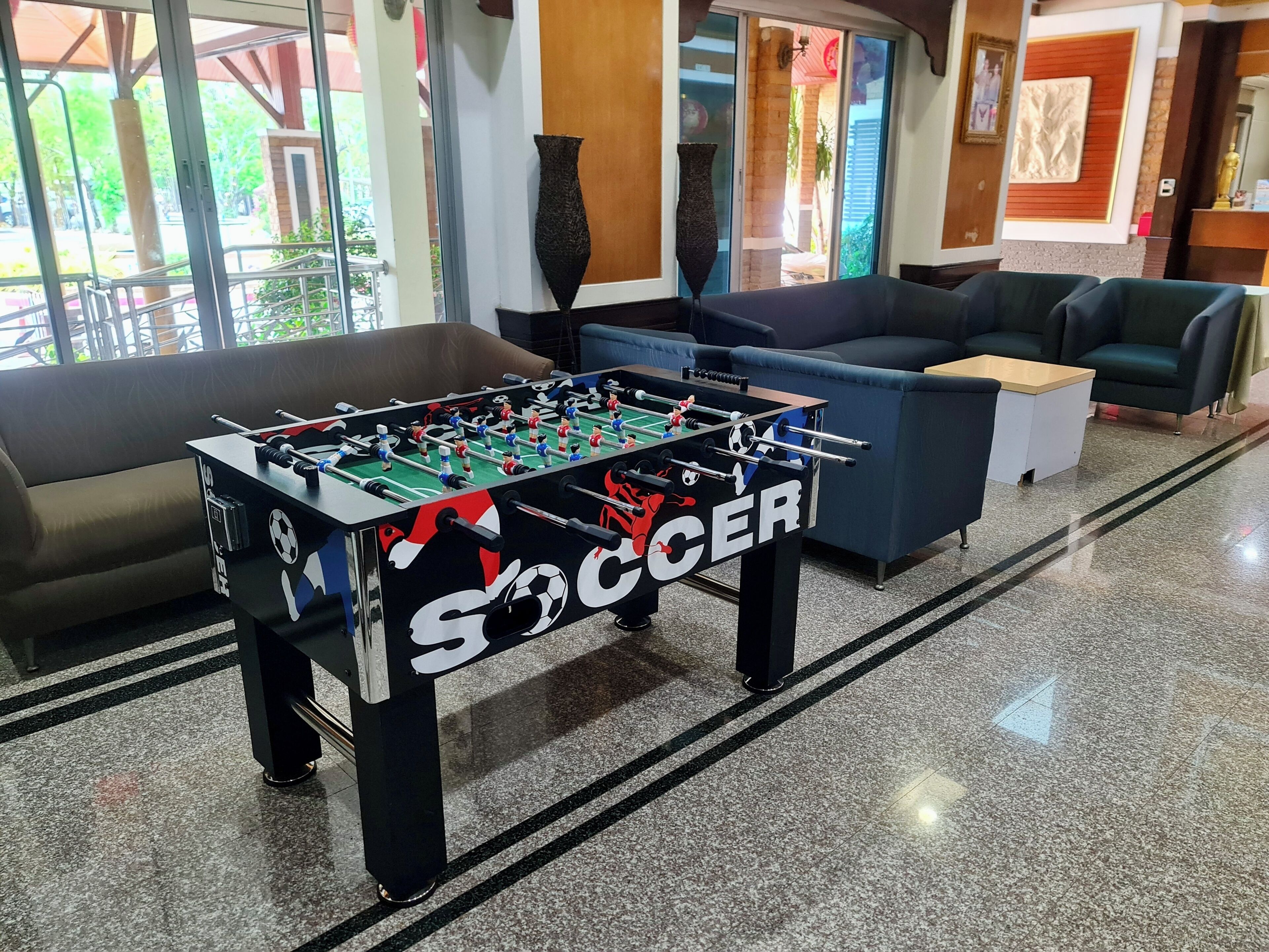 A foosball table labeled 'SOCCER' in a lobby with a sofa, a coffee table, and a view of the outdoors.