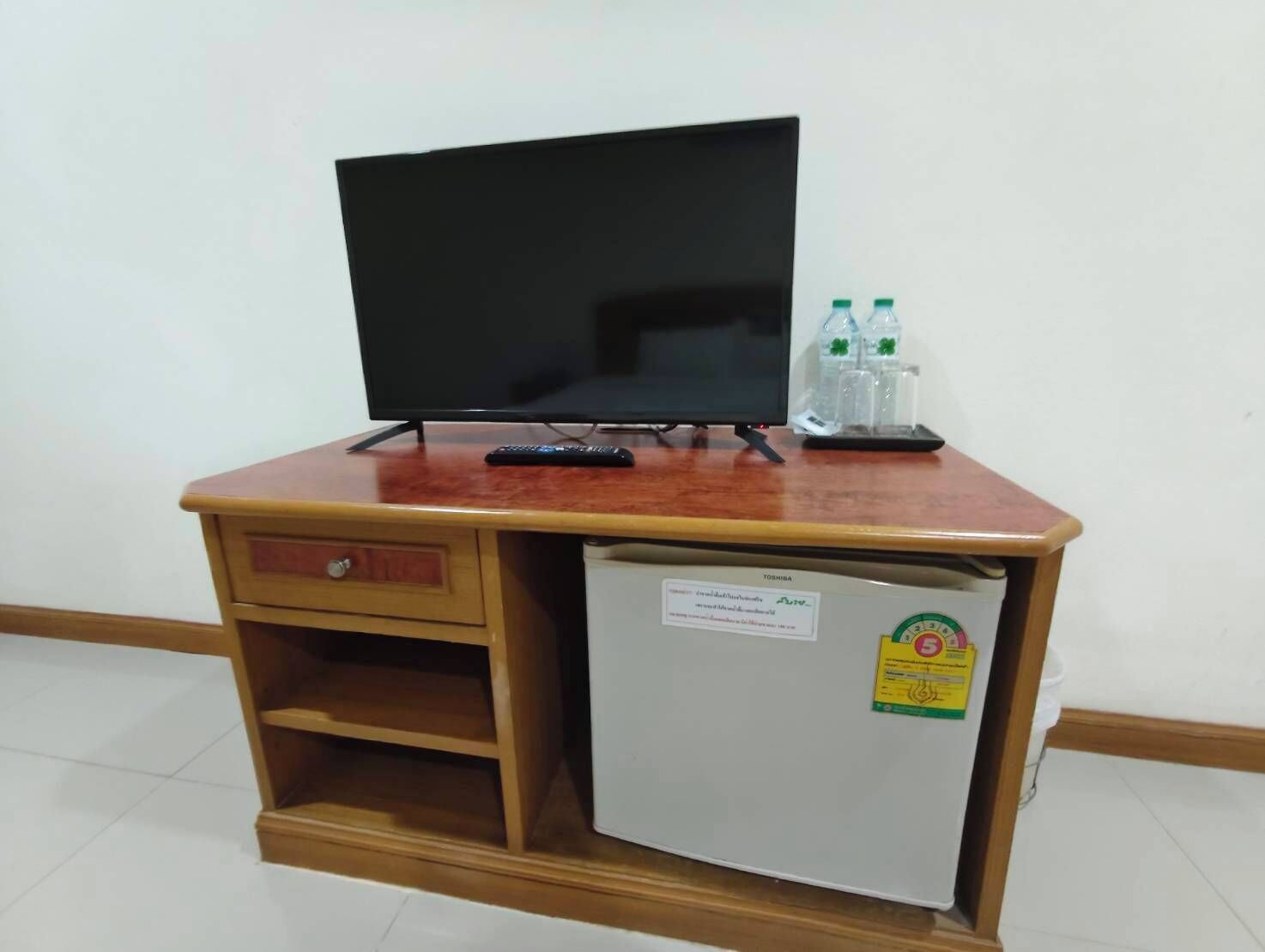 A wooden desk with a television, a small refrigerator, and two bottles of water.