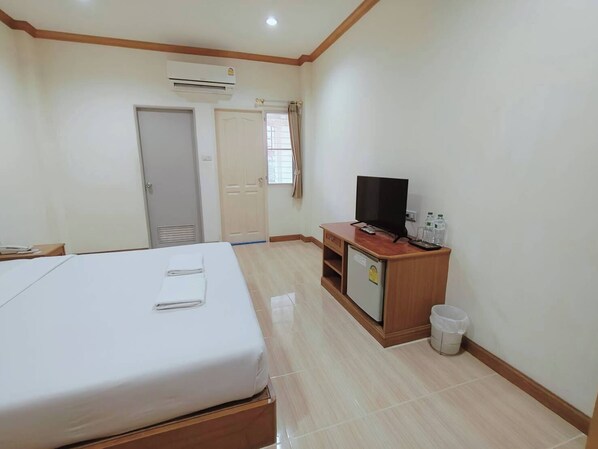 Una habitación de hotel con cama, escritorio con televisor, refrigerador pequeño y un cesto de basura.