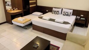 A hotel room with a large bed, a desk, a chair, a small table, and a mirror. - Sabai Hotel (Nakhon Ratchasima)