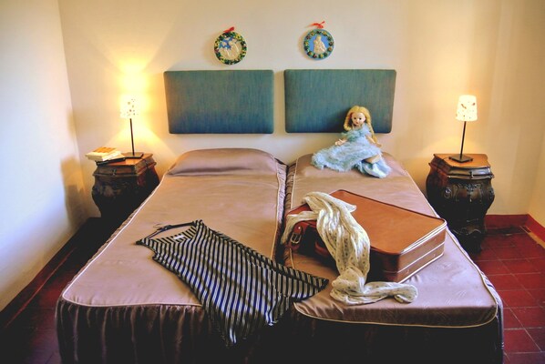 A double bed with a striped pillow, a doll, and a book on the bed. There are two nightstands with lamps and a wall with two framed pictures.