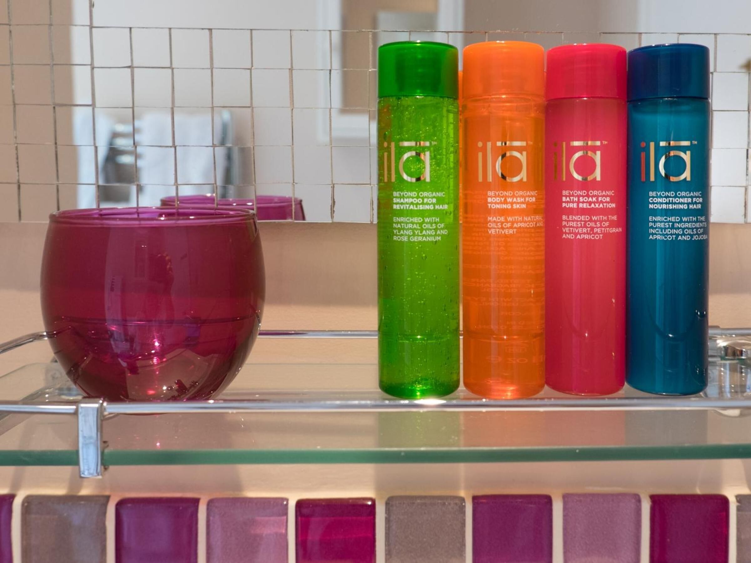 A shelf with four bottles of ILA organic hair care products and a purple candle.