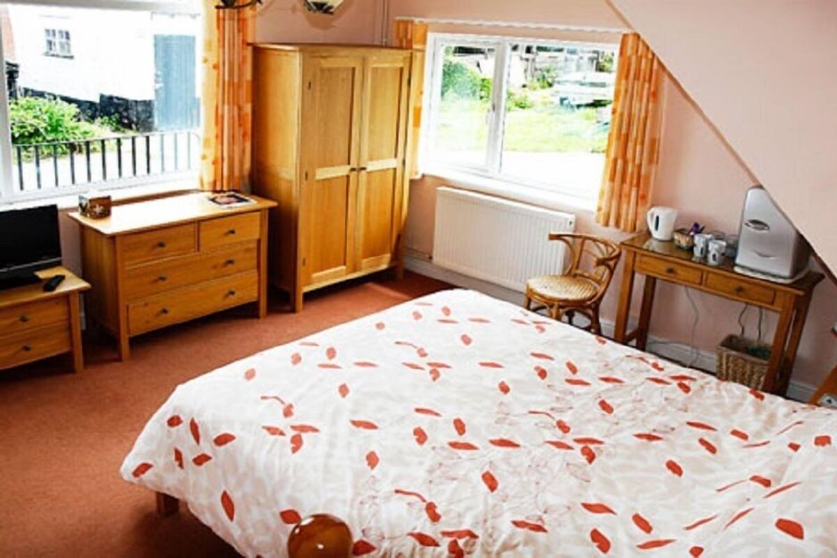 A bedroom with a bed, wooden wardrobe, desk, chair, and a radiator.