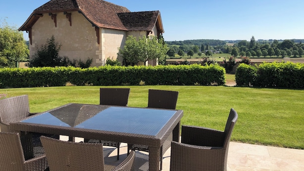 A patio with a table and chairs, a building with a tiled roof, and a view of a green landscape. - Gîte du Domaine de La Maison Neuve (Saint-Jean-Saint-Germain)