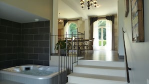 A modern bathroom with a large bathtub, a staircase leading to a dining area, and a chandelier. - Gîte du Domaine de La Maison Neuve (Saint-Jean-Saint-Germain)