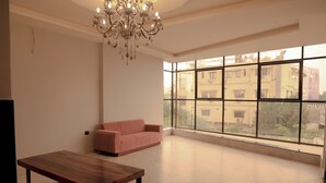 Ein geräumiges Zimmer mit einem großen Fenster, einem rosa Sofa, einem Holztisch und einer Chandelüster.