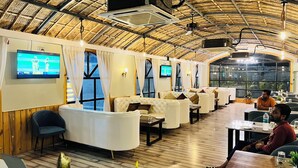 Ein Restaurant mit hohen, reetgedeckten Decken, gepolsterten Sitzgelegenheiten und mehreren Fernsehern an den Wänden.