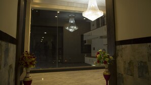 Eine Lobby mit einem Kronleuchter, zwei Blumenvasen und Blick auf ein modernes Gebäude durch eine Glastür.