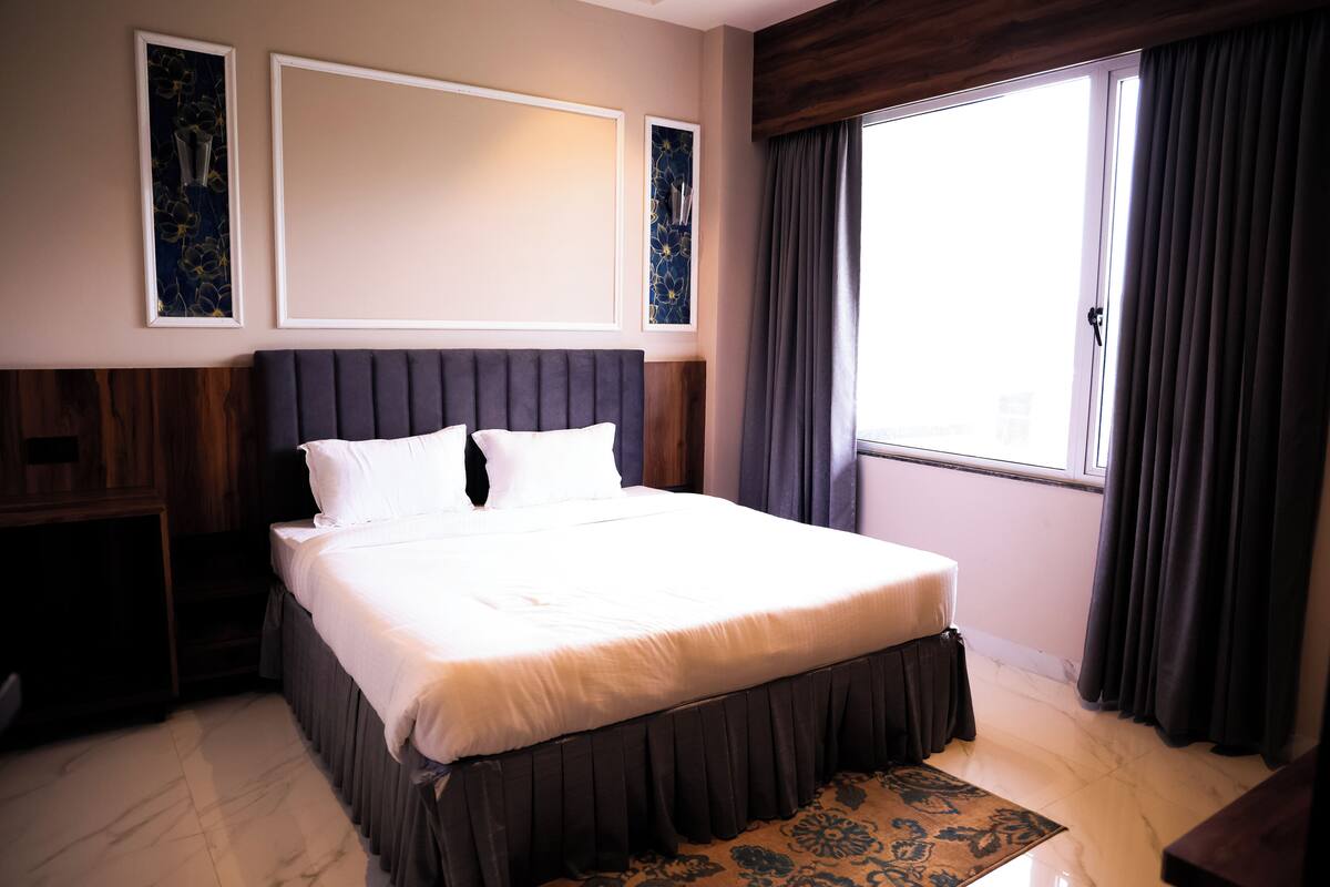 A neatly made bed with white linens, a dark headboard, and a wooden nightstand to the left.