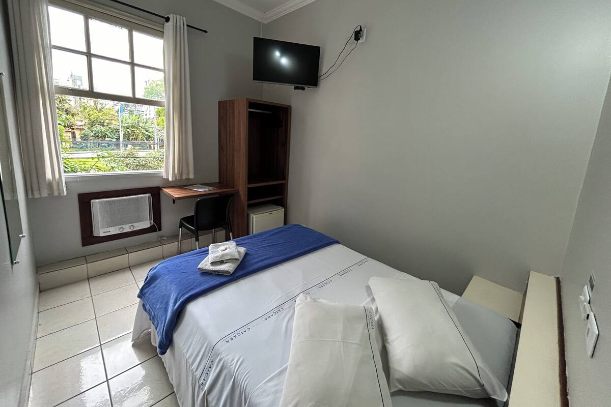 Quarto com cama, escrivaninha, cadeira, televisão e guarda-roupa.