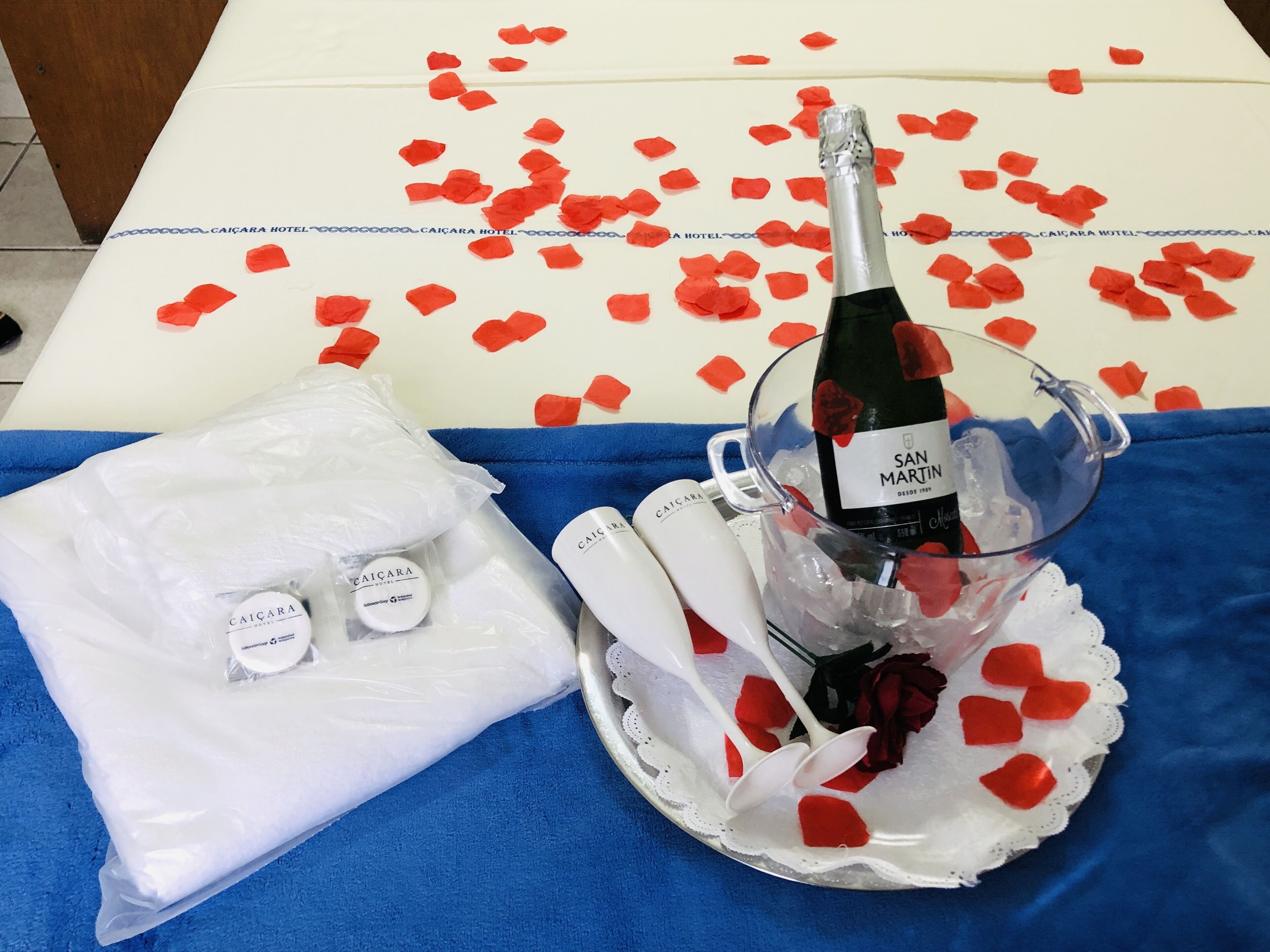 Un tavolo con una bottiglia di champagne, petali di rosa e un kit da toilette.
