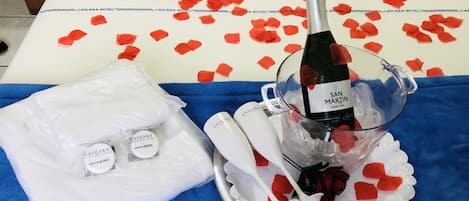 Un tavolo con una bottiglia di champagne, petali di rosa e un kit da toilette.