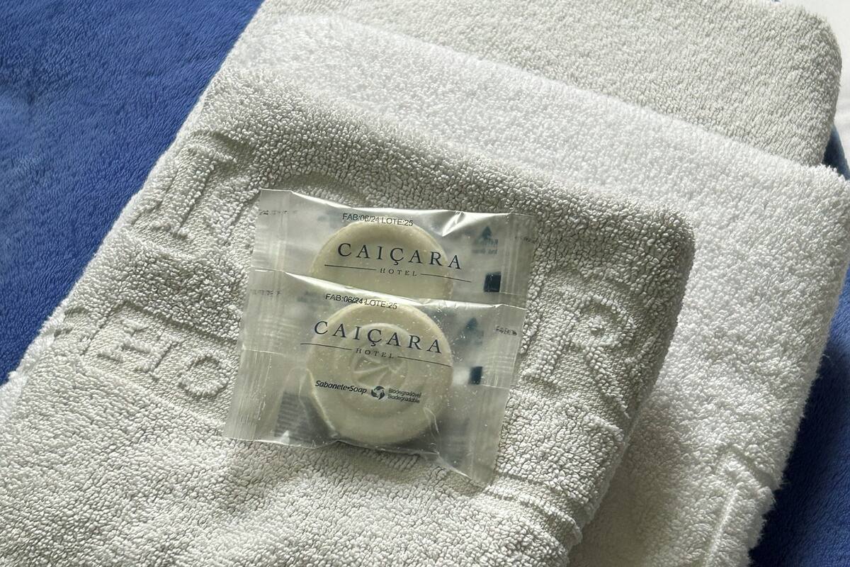 Toalha branca com um saquinho transparente identificado como "Caicara Hotel" e um sabonete.