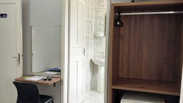 Quarto de hotel com escrivaninha, cadeira, televisão e um pequeno frigorífico.