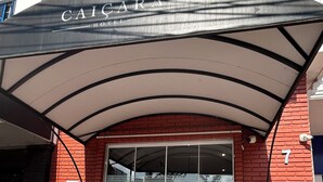 The exterior of Caicara Hotel with a modern design, featuring a glass entrance, red brick walls, and a covered entrance area. - Hotel Caiçara (Santos)