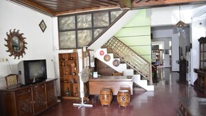 A spacious living area with a wooden cabinet, a television, a fan, and two drums. - Sartika Hotel (Yogyakarta)