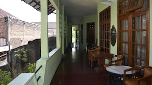 A corridor with a tiled floor, wooden furniture, and a brick wall on one side. - Sartika Hotel (Yogyakarta)