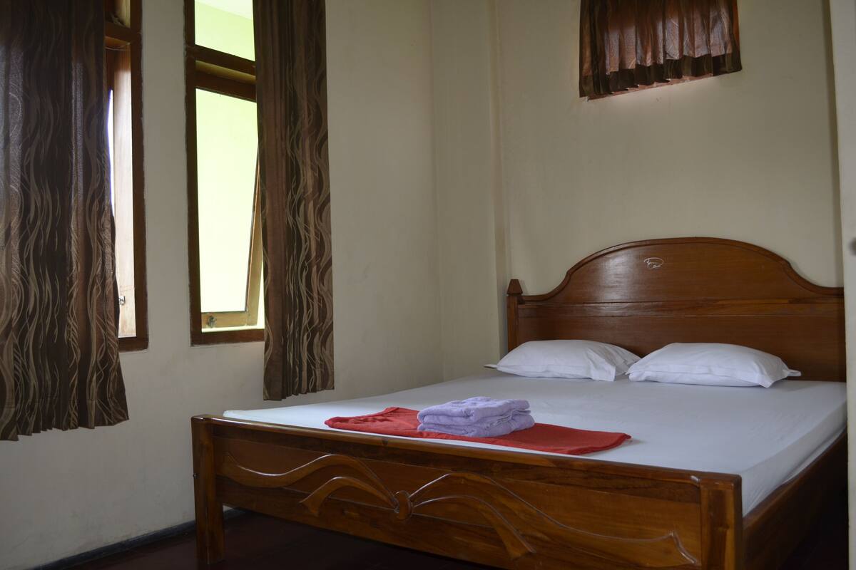 A single bed with a wooden frame, two white pillows, and a red and purple towel on the bed.