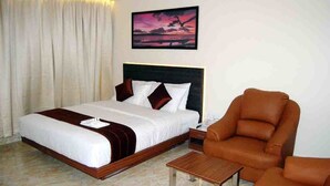 A hotel room with a bed, a chair, a small table, and a painting on the wall. - Haywizz Port Blair - Port Blair (Port Blair)