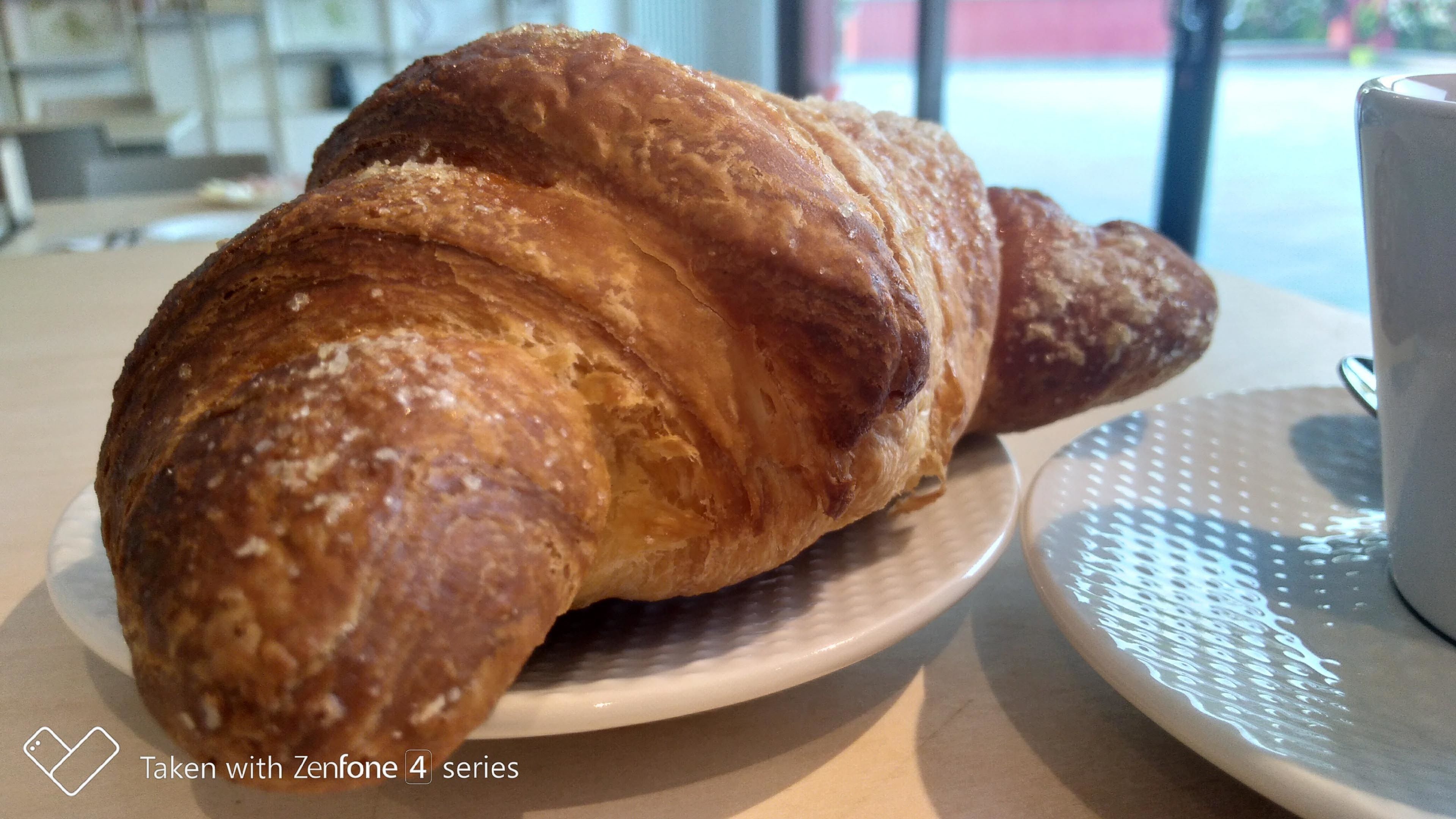 Un croissant sobre un plato blanco con una taza de café en un platito.