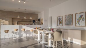A modern kitchen with white countertops, a dining area with a white table and chairs, and a bar area with stools. - Agriturismo La Biòca (Serralunga d'Alba)