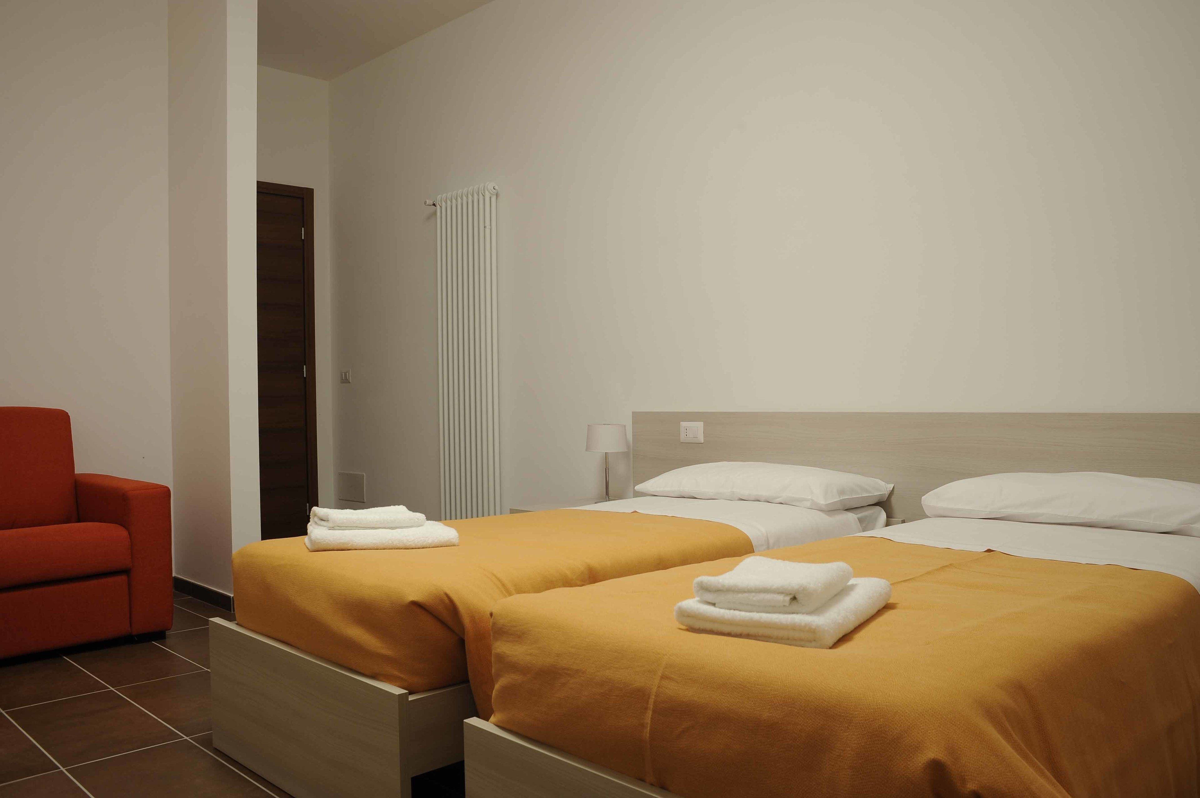 A hotel room with two beds, a red chair, and a radiator.