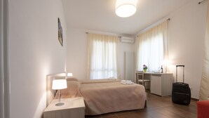 A hotel room with a bed, bedside table, lamp, desk, chair, and a suitcase. - Agriturismo La Biòca (Serralunga d'Alba)