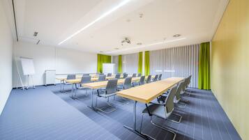 A conference room with long tables, chairs, a whiteboard, and a projector.