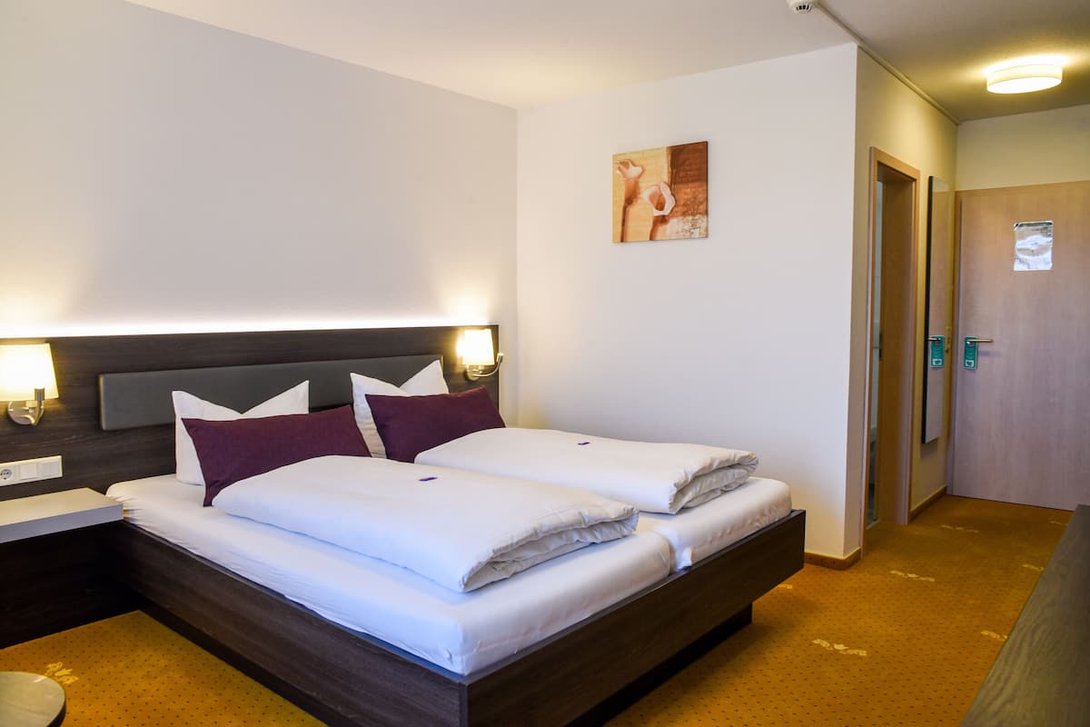 Ein Hotelzimmer mit zwei Betten, einem Nachttisch, einer Wandlampe und einer Tür zum Badezimmer.