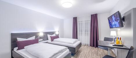 A hotel room with two beds, a desk with a chair, a television, and a window with curtains.