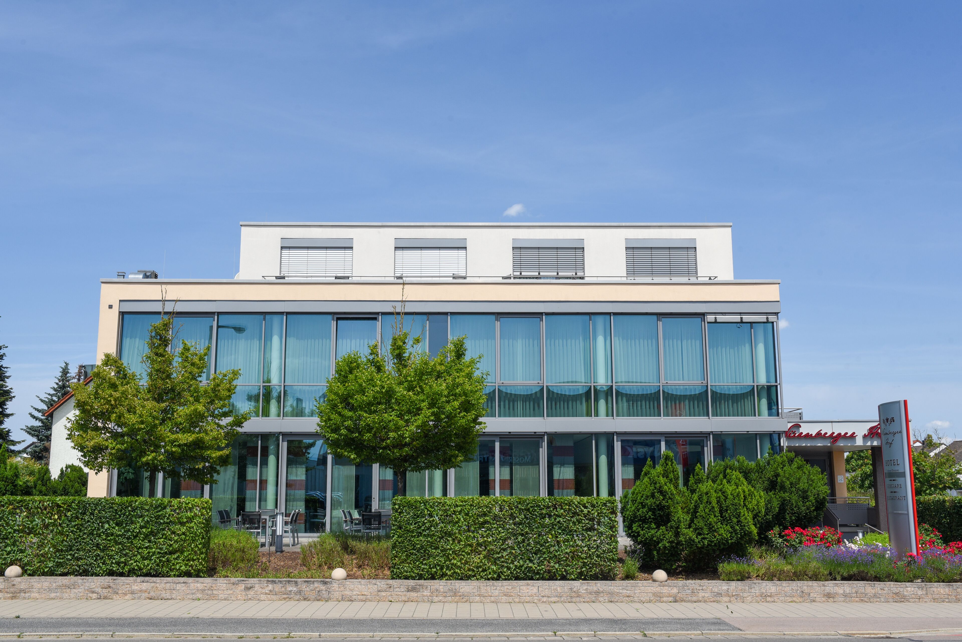 Un hôtel moderne doté d’une façade en verre, d’un espace extérieur aménagé pour s’asseoir et d’un jardin paysager.