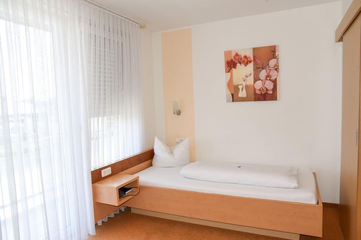 Ein Einzelbett mit Holz-Kopfteil, ein kleiner Nachttisch und eine Wandleuchte.