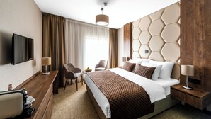A modern hotel room with a large bed, a flat-screen TV, a desk with a coffee maker, and a seating area with a chair and table. - Amsterdam Hotel (Belgrade)