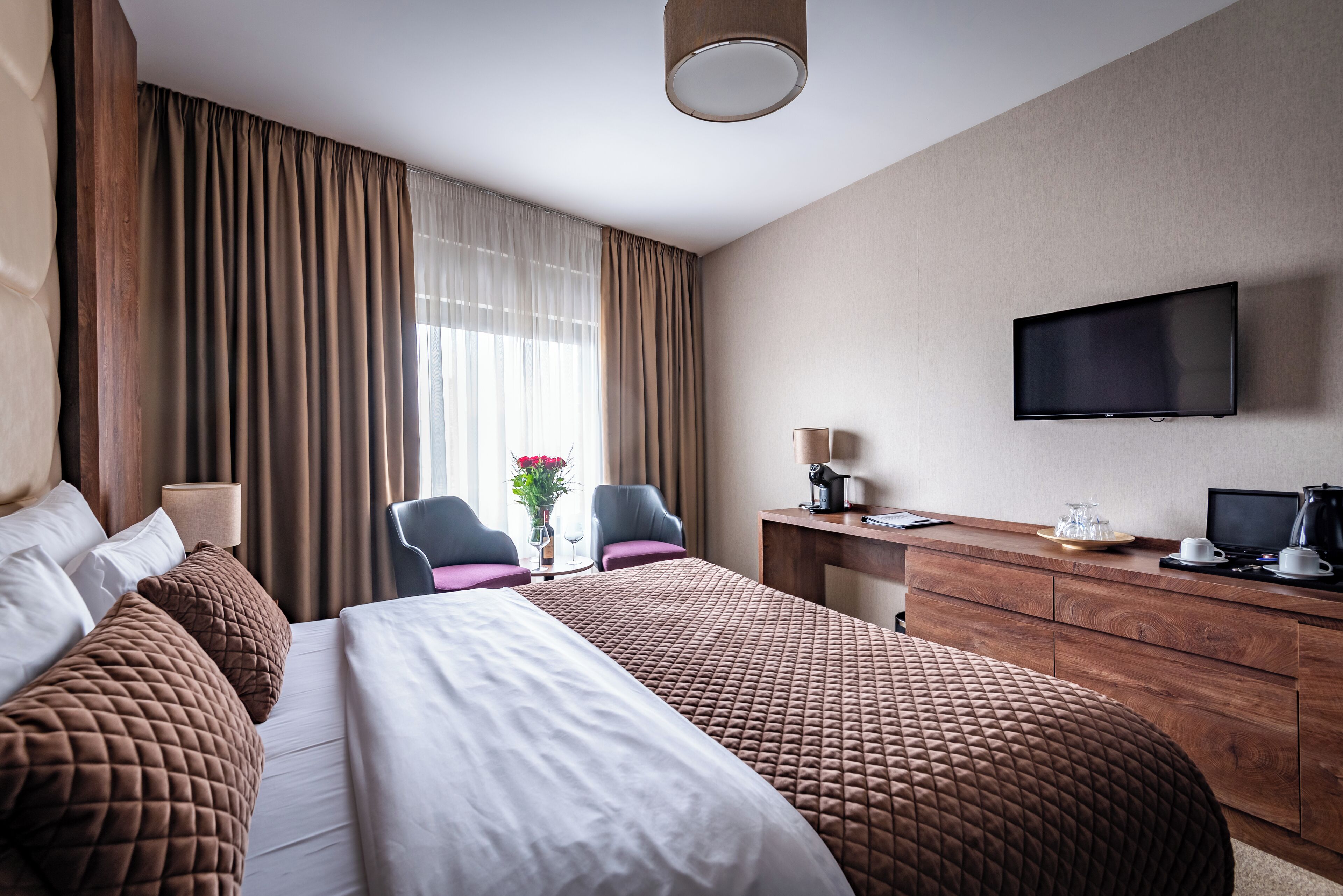 A hotel room with two beds, a desk, a chair, a television, and a window with curtains.