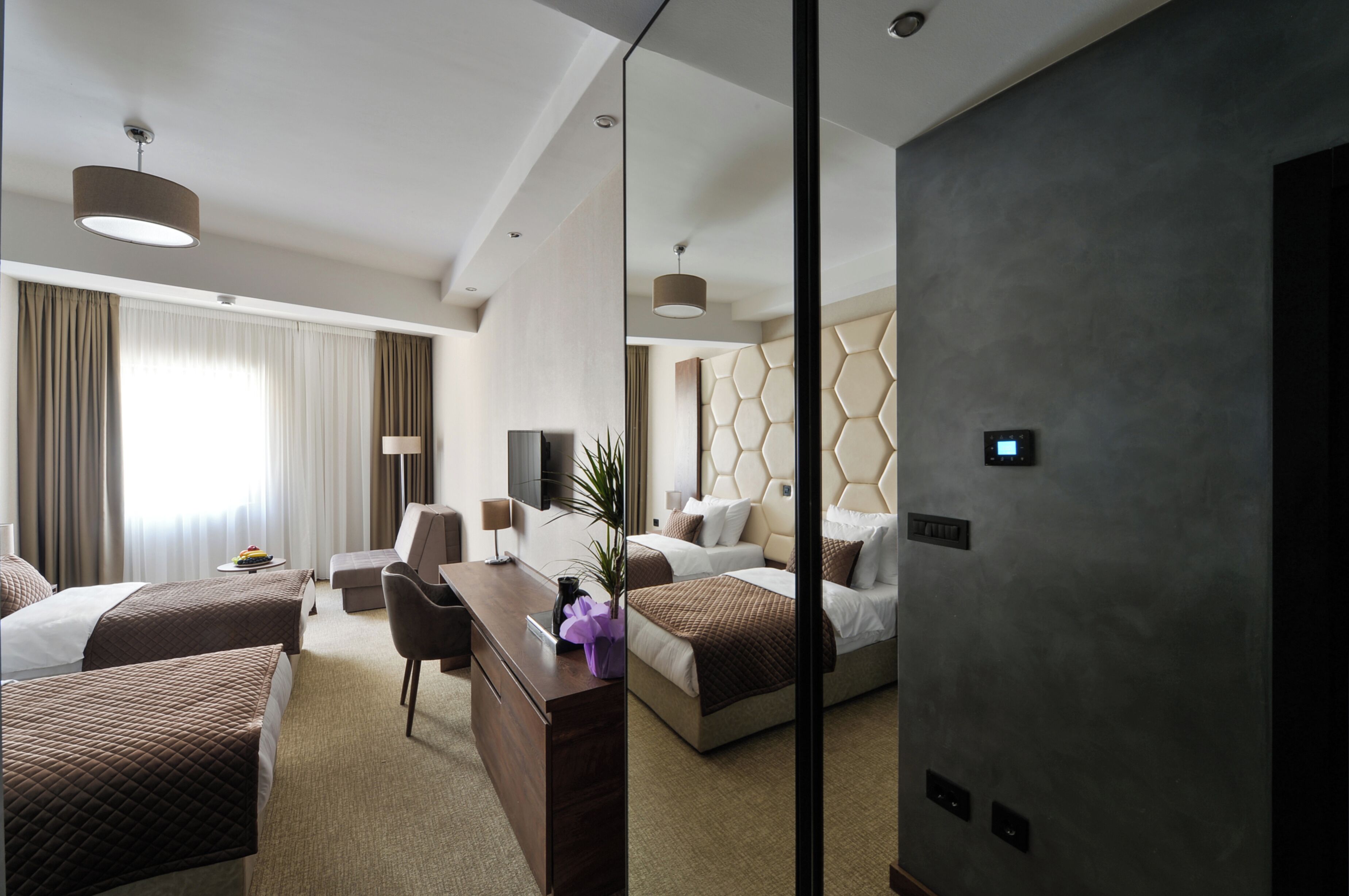 A hotel room with two beds, a desk, a chair, and a large mirror.