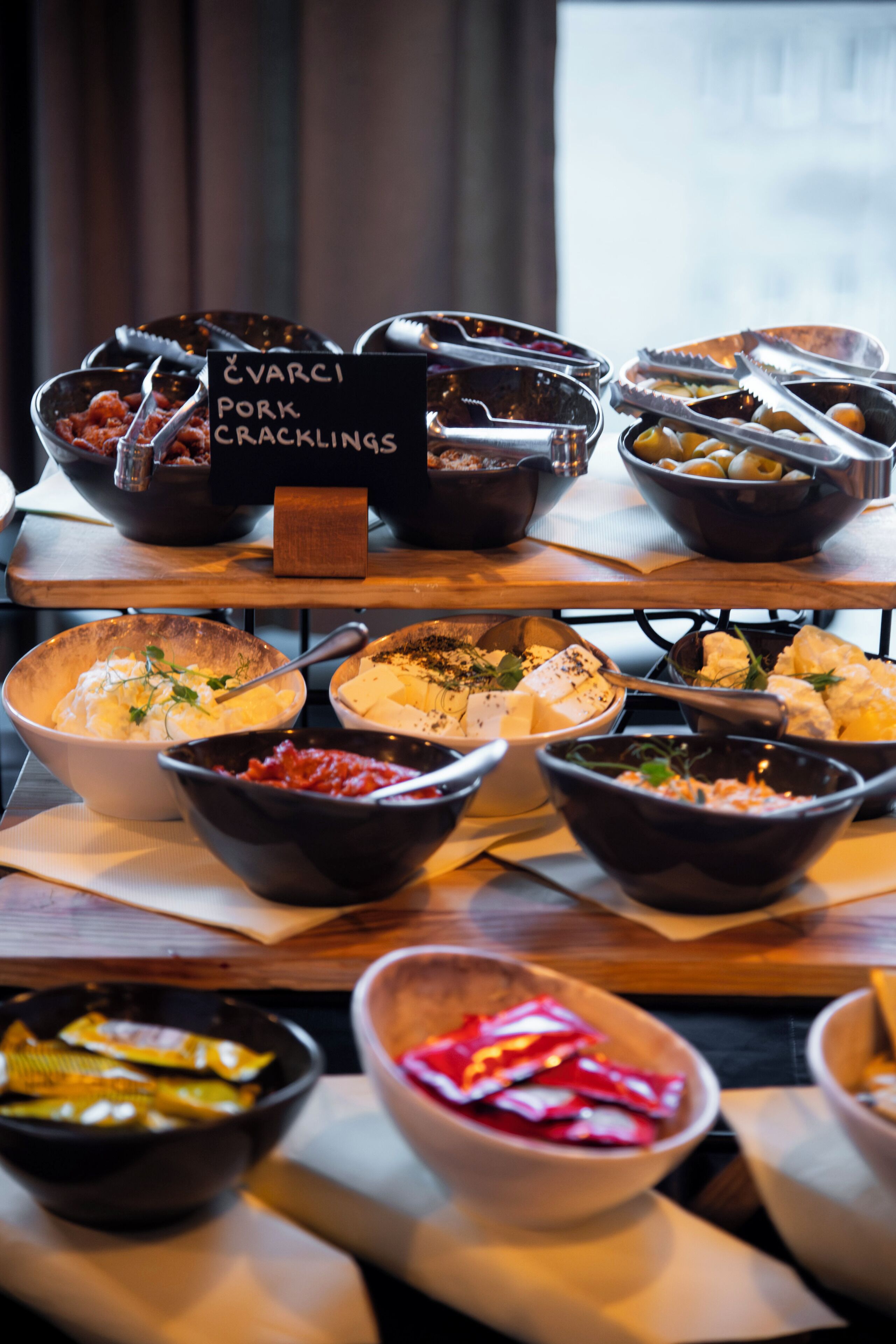 Une table de buffet proposant divers plats, notamment des grattons de porc, du fromage et des légumes.