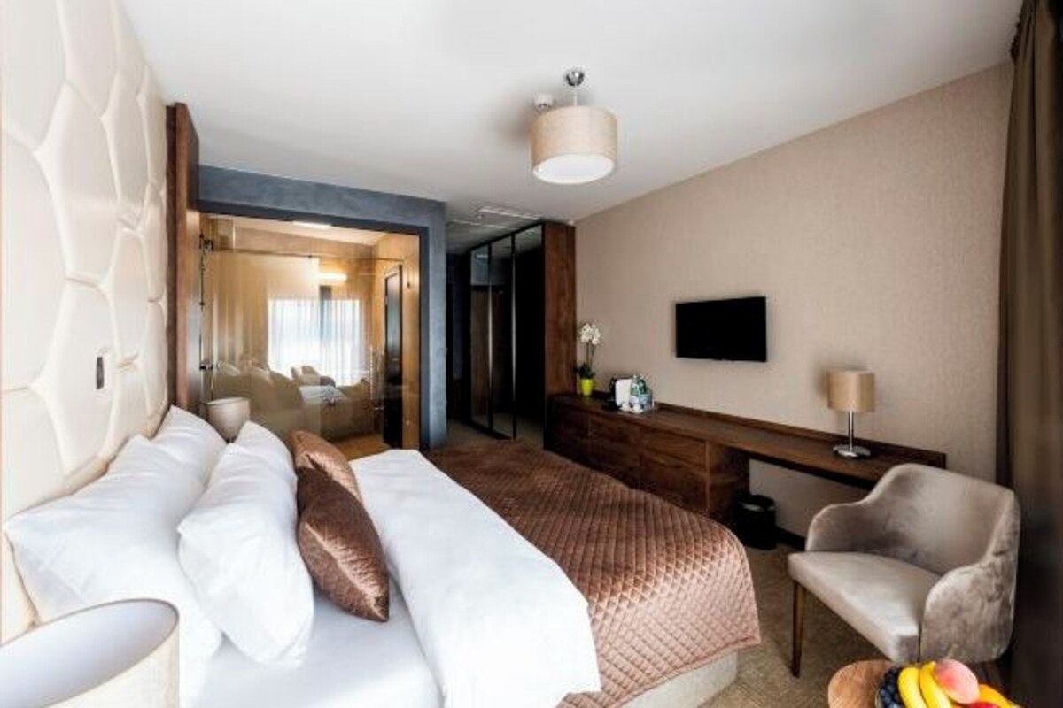 A hotel room with a bed, a desk, a chair, a TV, and a mirror.