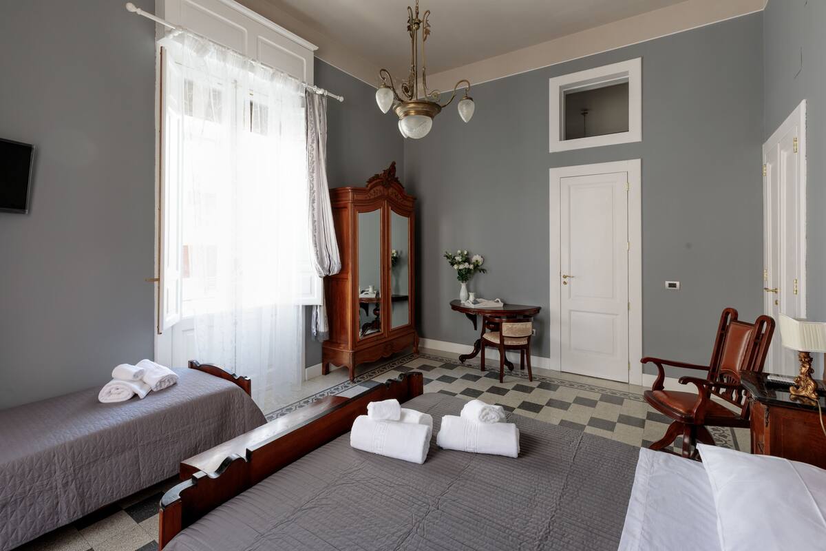 Een hotelkamer met twee enkele bedden, een houten dressoir, een stoel, een bureau, een spiegel en een kroonluchter.