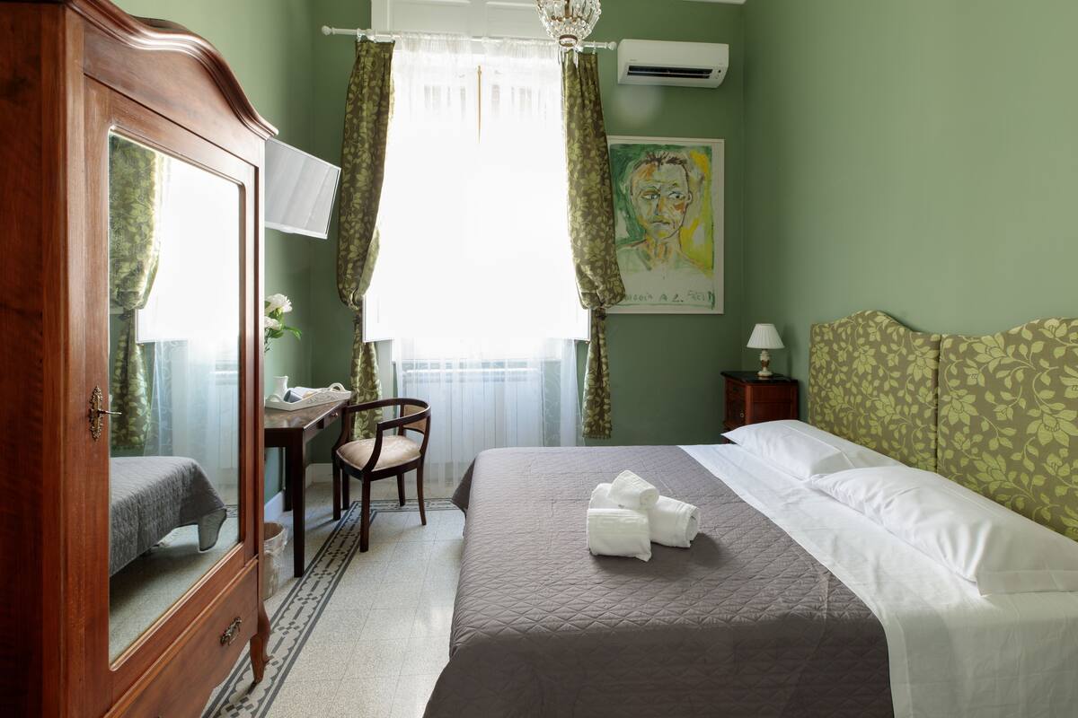 Een hotelkamer met een bed, een houten kledingkast, een bureau met stoel en een schilderij aan de muur.
