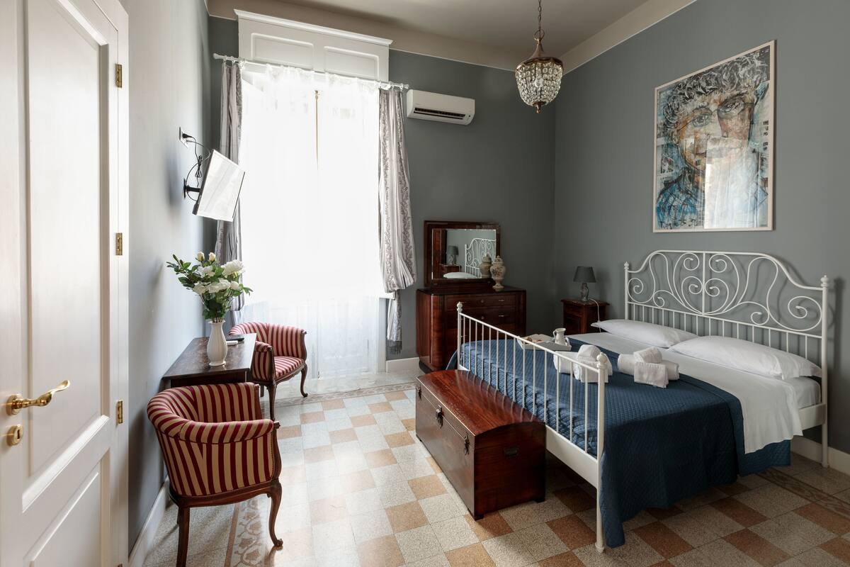 Een slaapkamer met een bed, een bureau, een stoel, een dressoir en een hangende lamp.