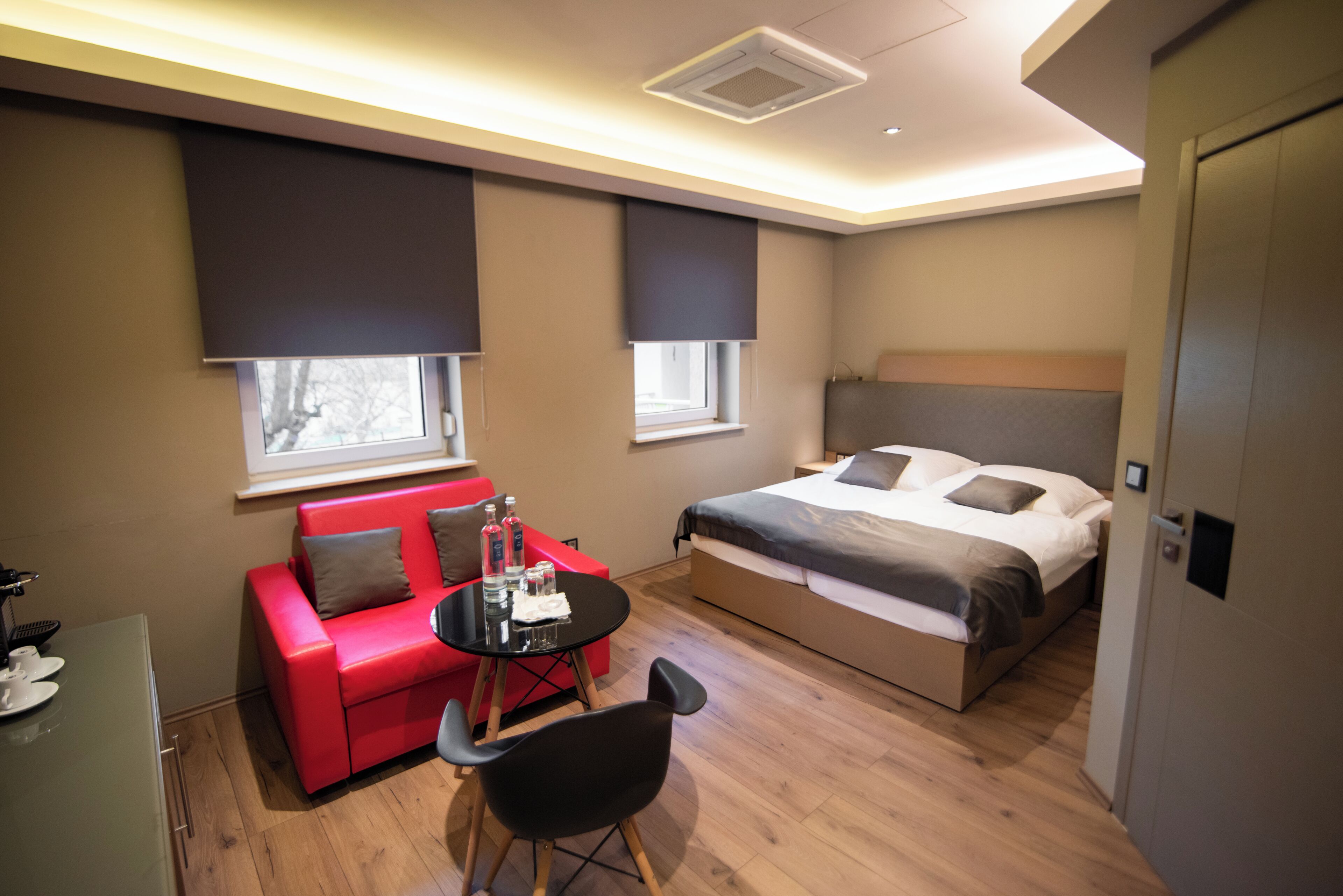 Una habitación de hotel moderna con una cama, un sofá rojo, una mesita y un escritorio.