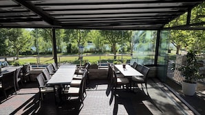 Une terrasse extérieure avec des tables et des chaises, un espace abrité et une vue sur la verdure et une route.
