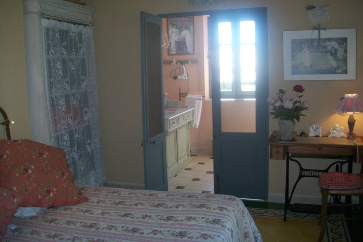 A bedroom with a bed, a chair, a desk, and a door leading to a bathroom.